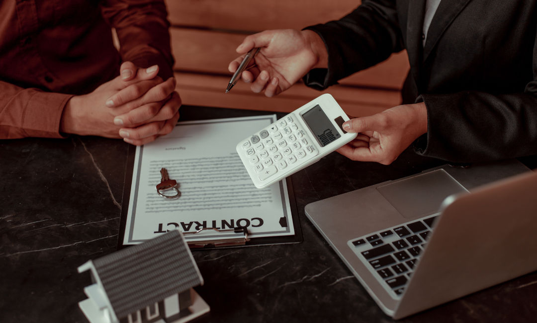 Close up of a contract and calculator with a salesperson explaining terms to the buyer.