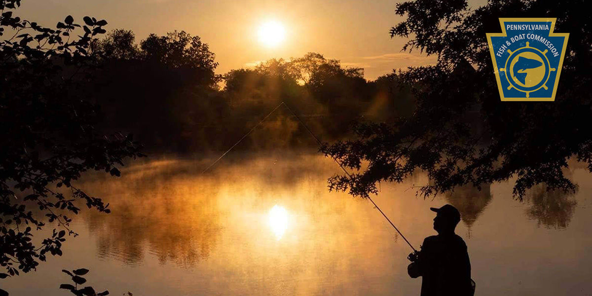 Silhouette of a man fishing along the shoreline of a lake at sunset