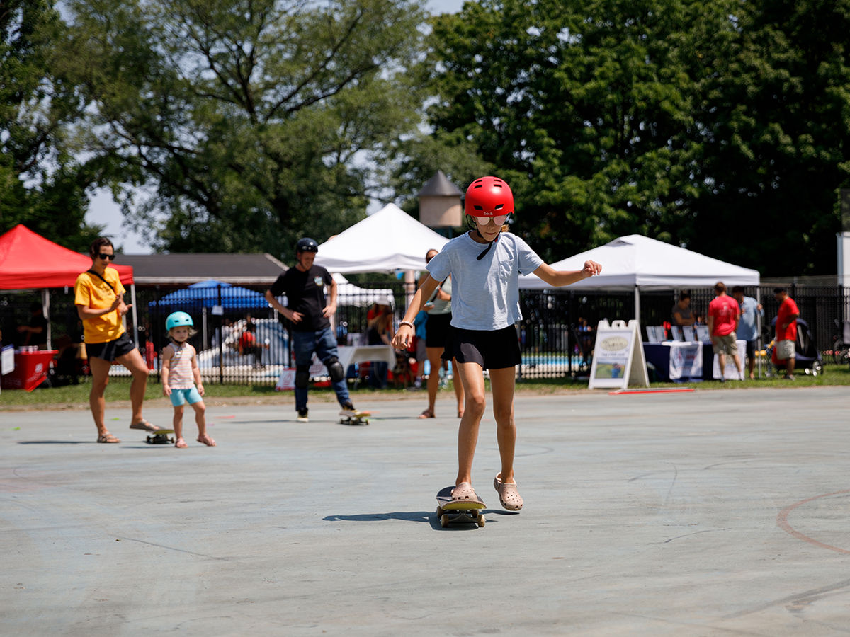 A young person skateboards in front of multiple pop-up tents.
