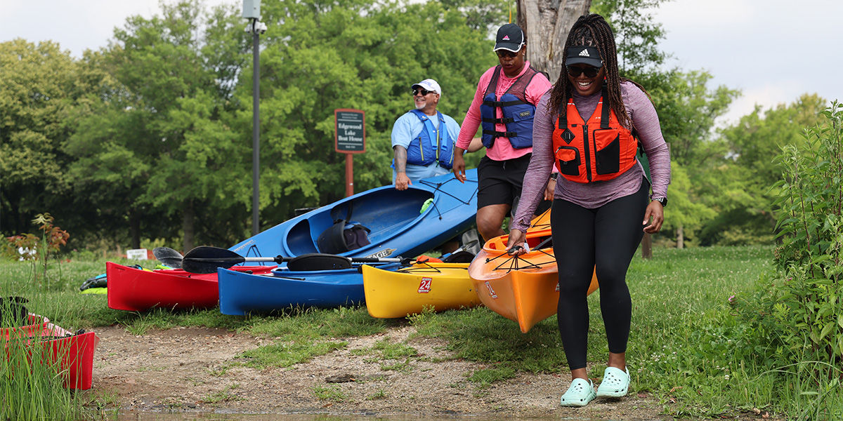 Two women wearing life jackets while carrying a kayak to the edge of a lake to prepare to launch.