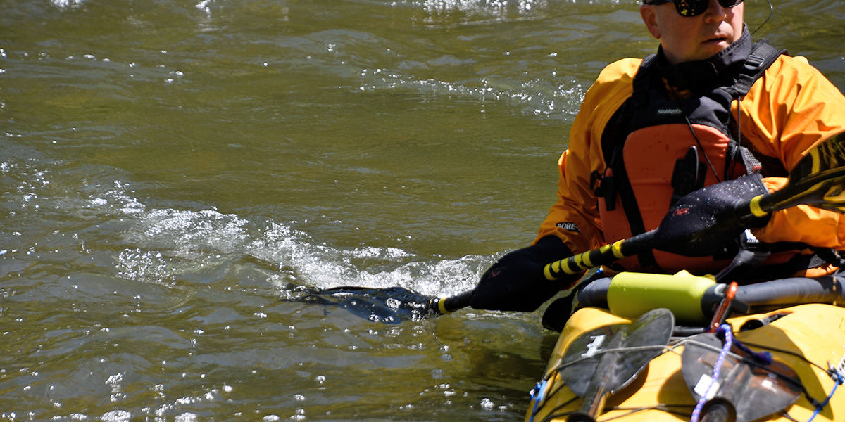 Man wearing a life jacket and cold weather gear uses his paddle to turn his kayak in the water