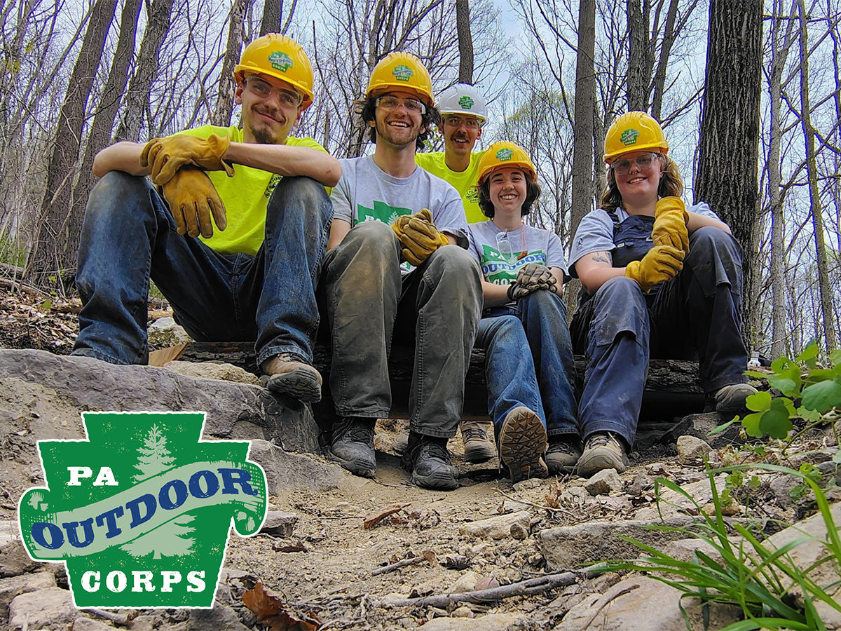 A group of PA Outdoor Corps workers pose for a group photo. The PA Outdoor Corps logo appears in the lower left corner.