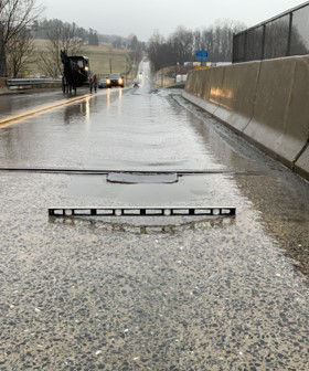 An image of a two-lane, roadway with several cars following an Amish horse and buggy on the left-hand side and a metal level sitting in the middle of the roadway on the right-hand side showing a visible trough in the roadway. 