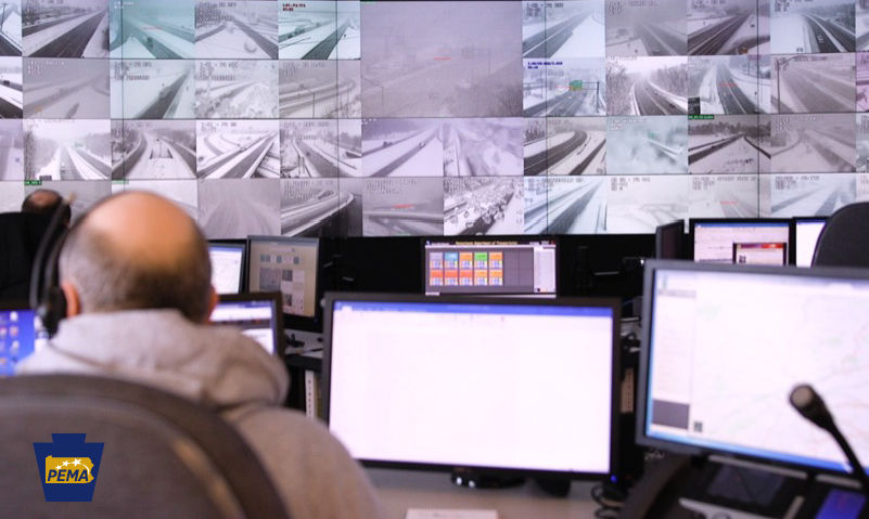 Two men in neon safety vests walk among a street full of downed telephone poles. 