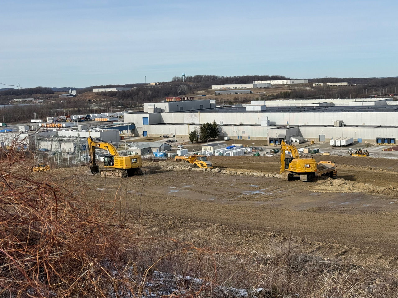 an image of two yellow bulldozers moving dirt and leveling the ground. A large distribution facility sits in the background.