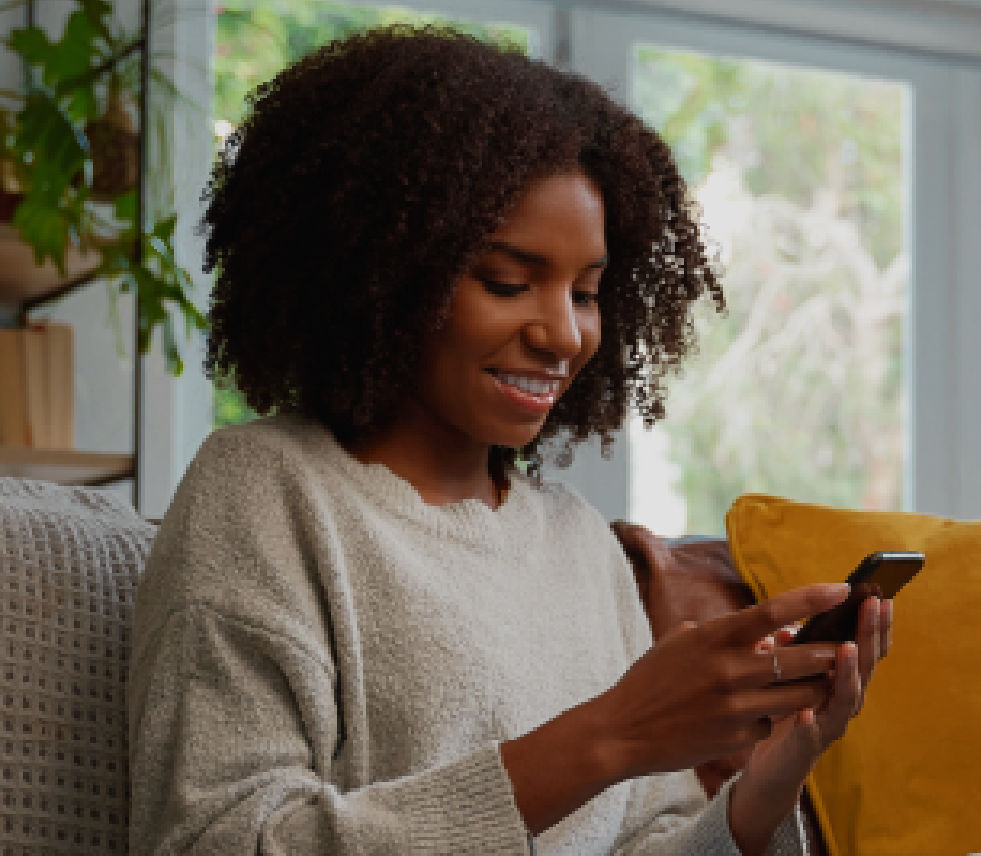 A woman sits on a couch while checking her phone.