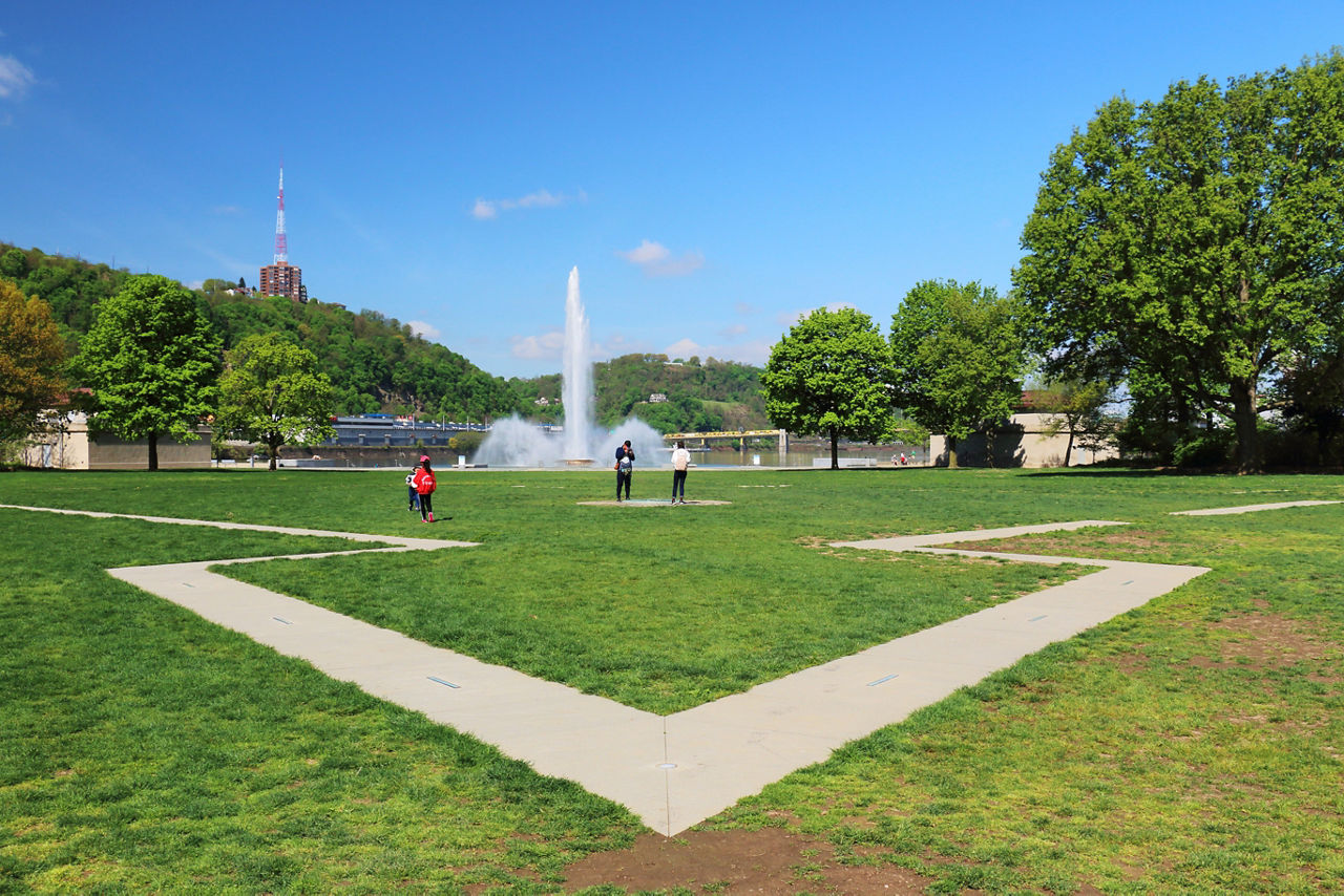 A tracery on the grass with trees and the iconic fountain in the background