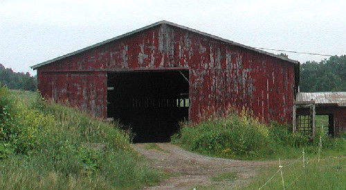 One story wood barn with large central opening under a front facing gable roof.