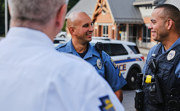 Uniformed police officers talk in front of marked police vehicles