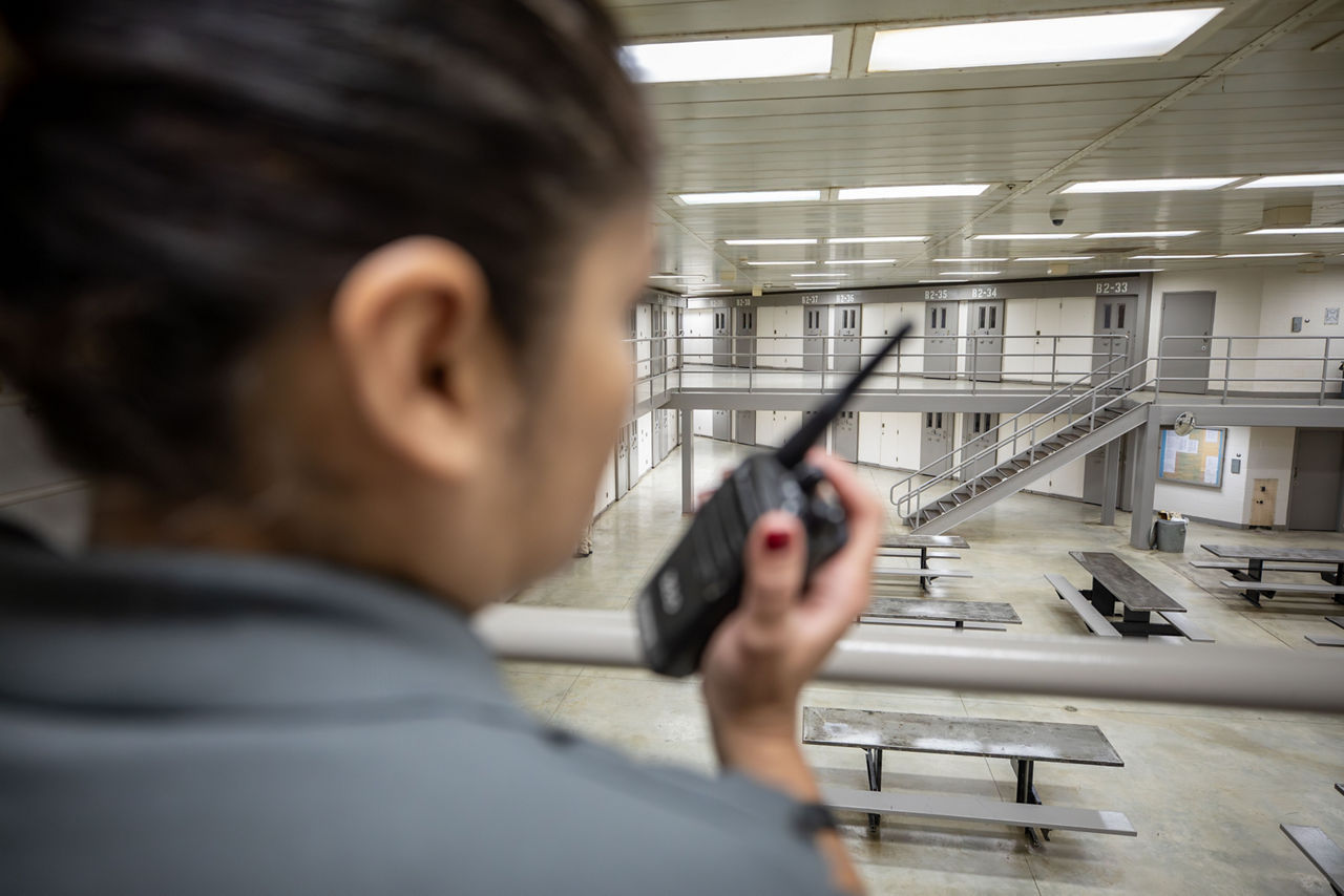 A corrections officer speaks into her radio while looking at a housing unit