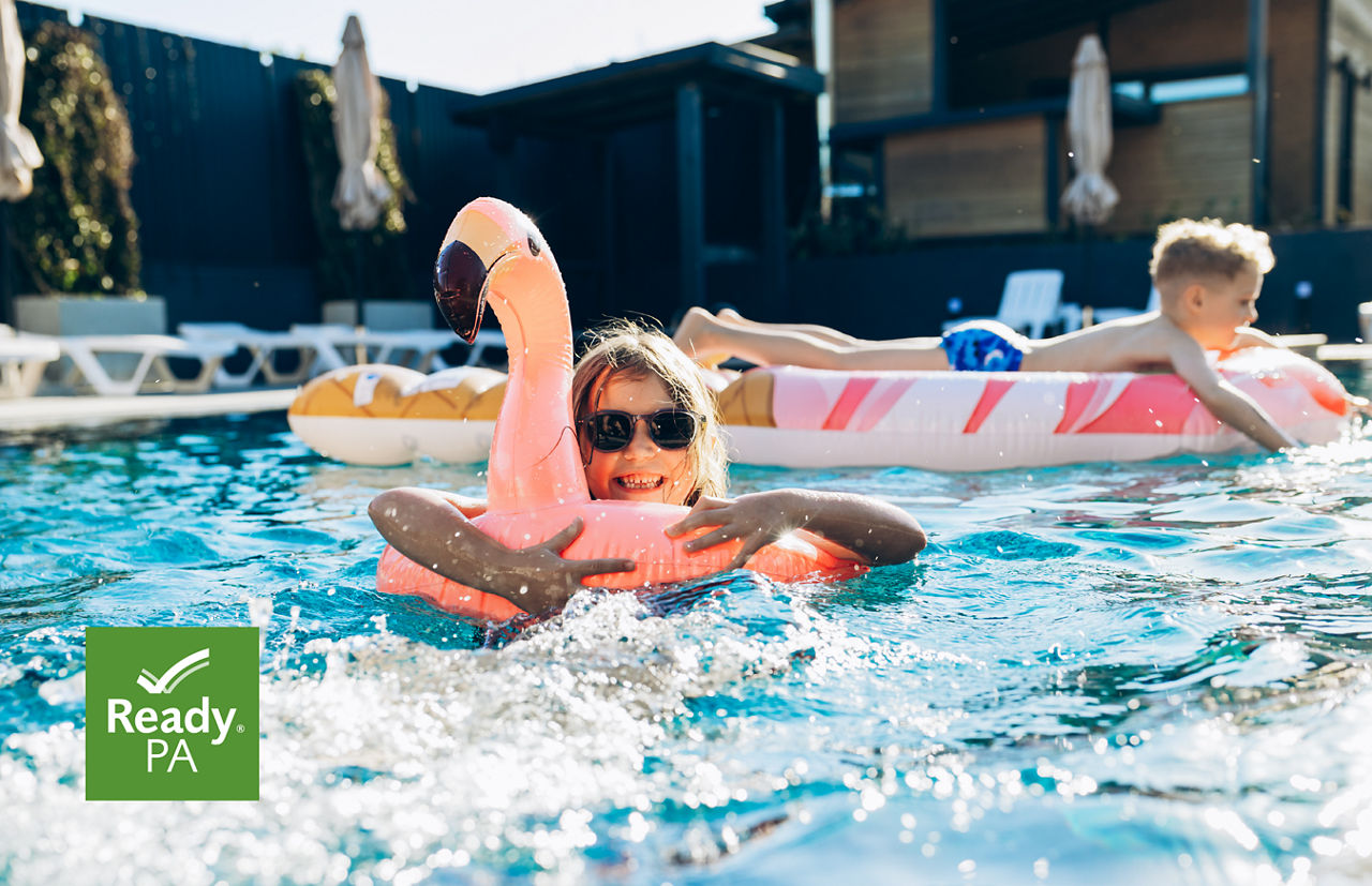 A blond girl hugs a flamingo float while splashing in a pool of clear, blue water.