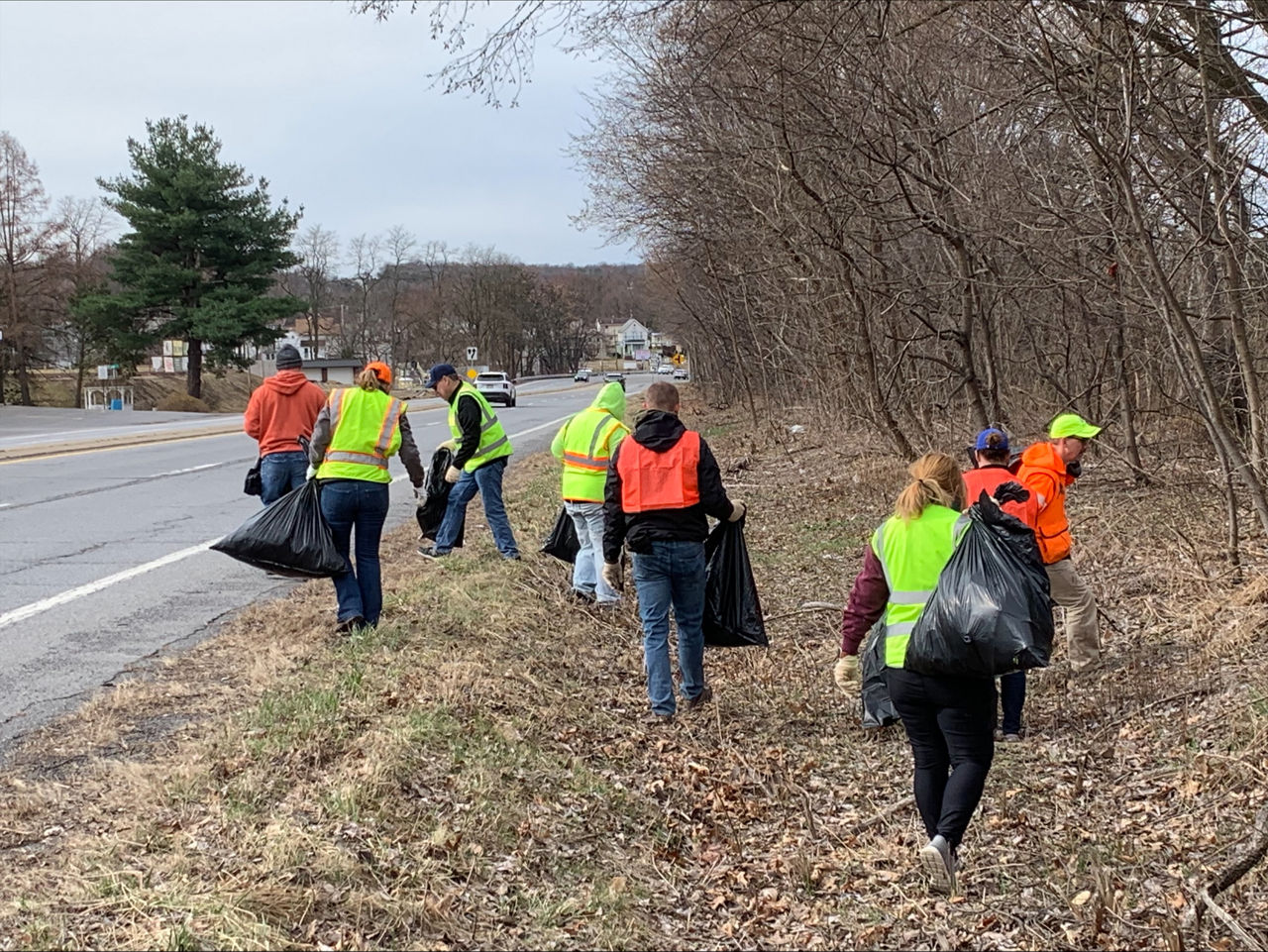 Group of people in high-vis vests, carrying trash bags, picking up trash along a roadway.