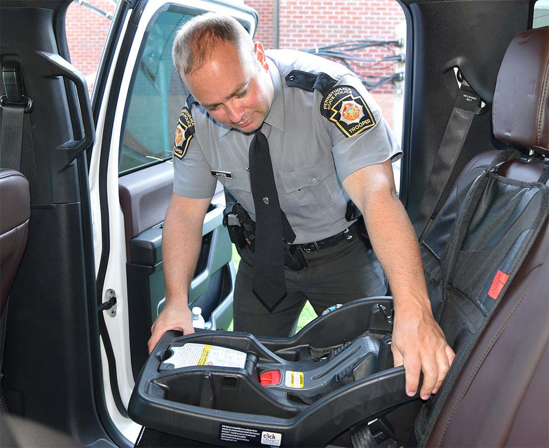 A uniformed PA State Trooper installs a car seat base in the back seat of a vehicle