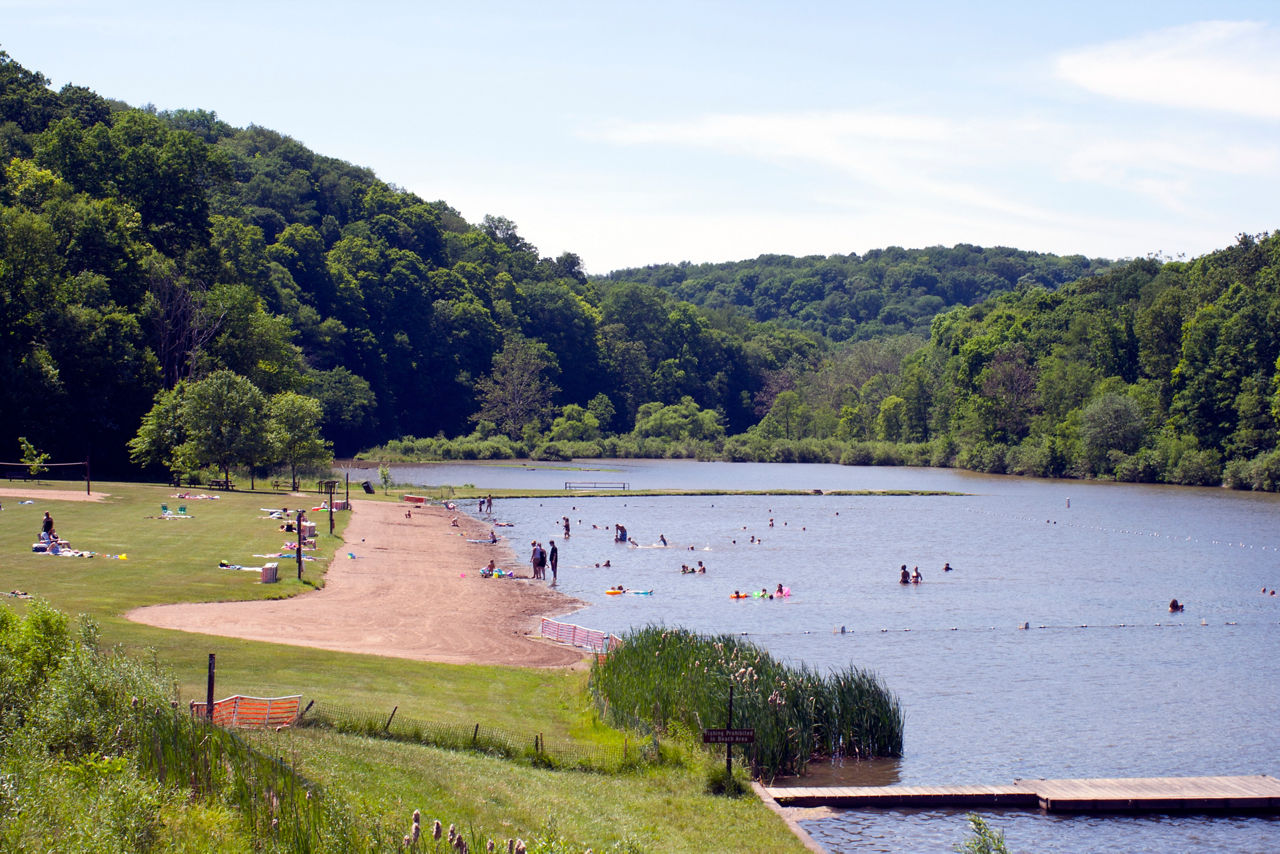 A sand swimming are on the side of the lake with forest in the background