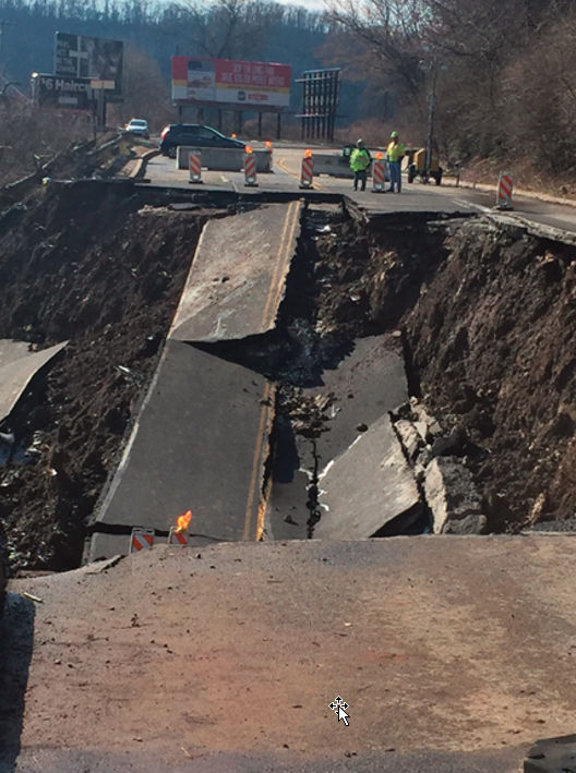 Large section of roadway collapsed; traffic blocked off as workers stand by.