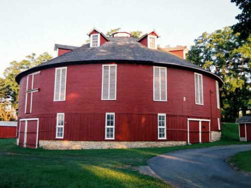 Two-story round red building with evenly spaced windows and louvers all around and rooftop dormers.