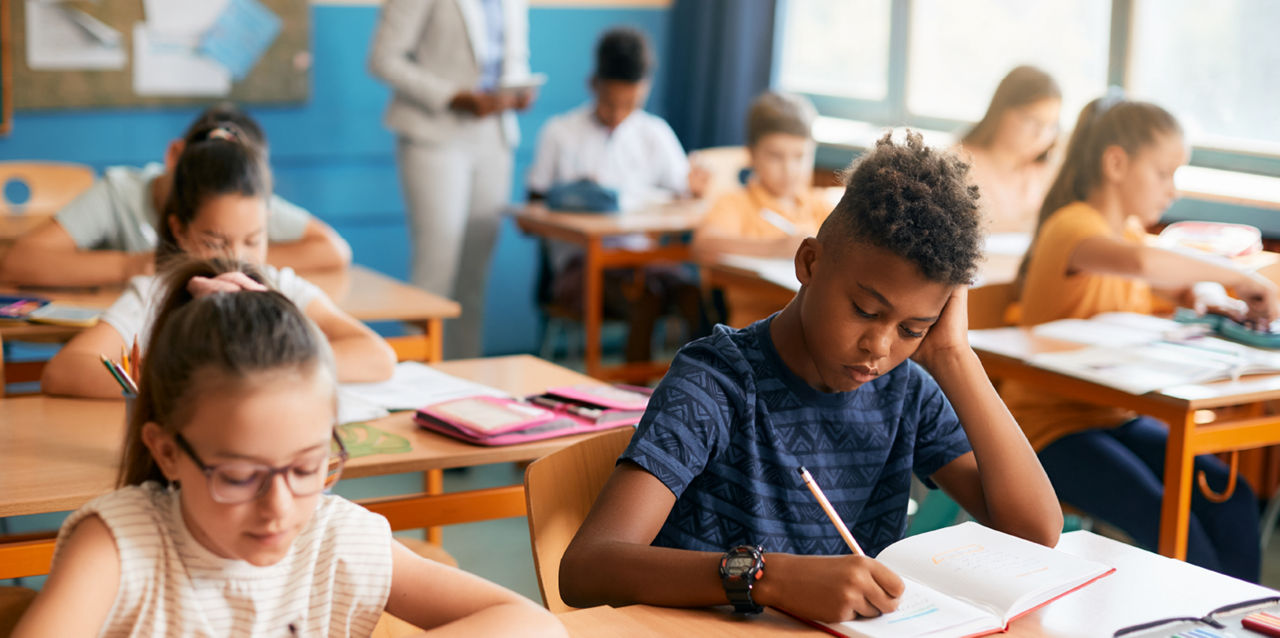 A classroom full of students at desks who are writing notes.