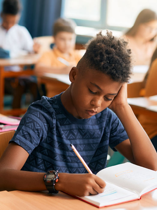 A young boy writes notes at his school desk.