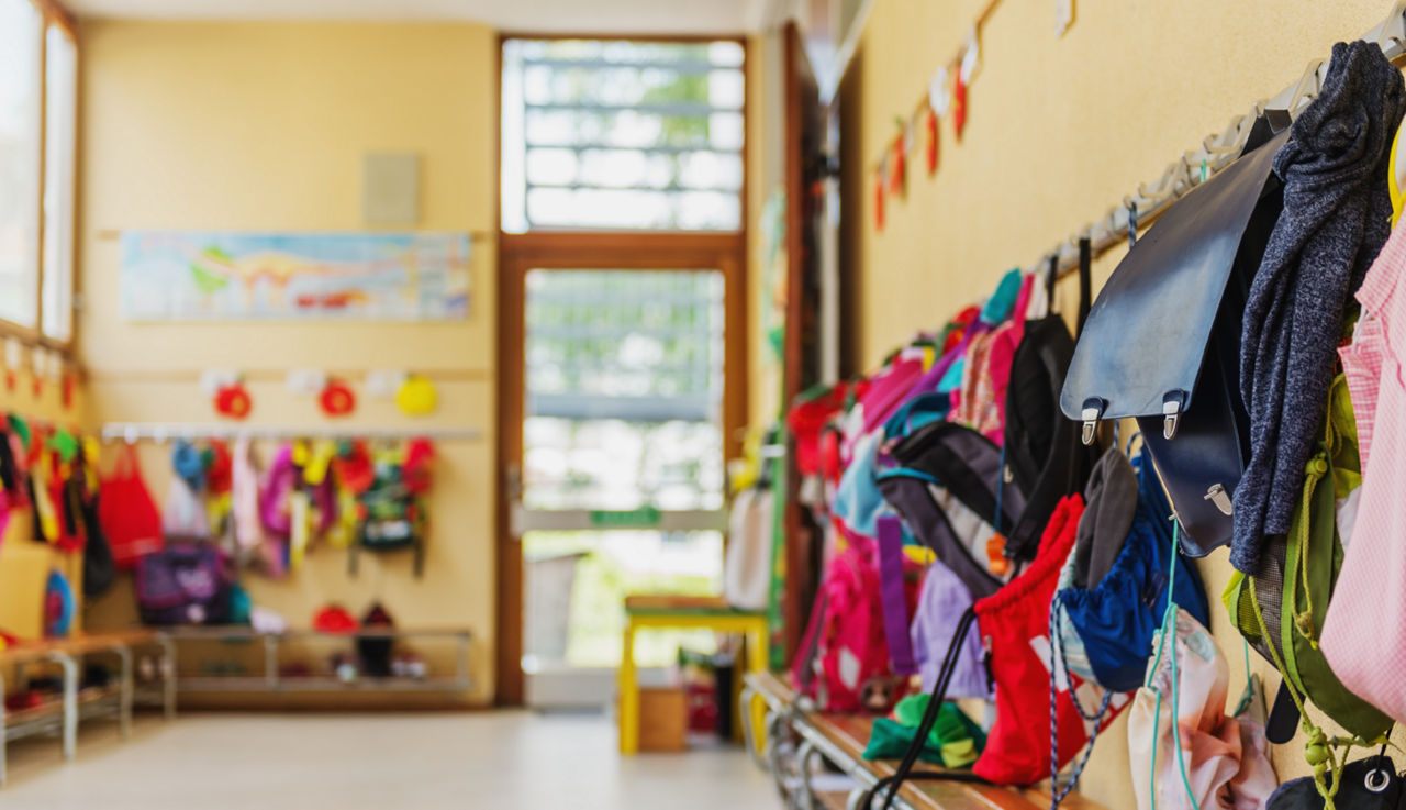 Children's belongings hang in the hallway of a classroom.