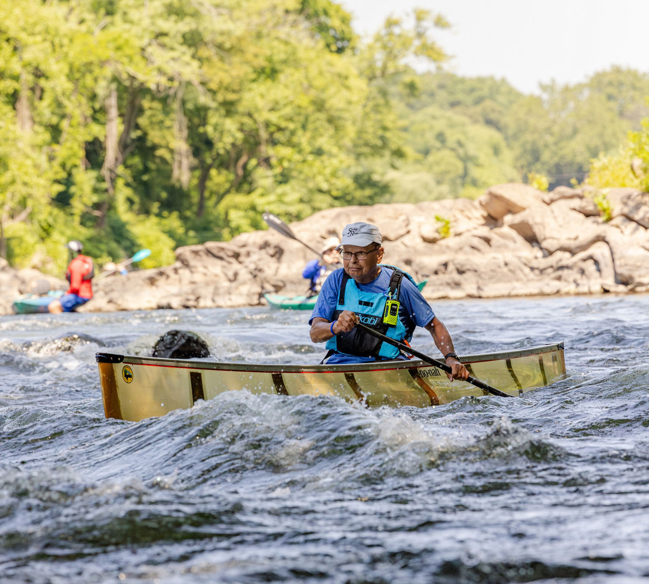 A man wearing a life jacket paddling a canoe through small rapids along the Schuylkill River.