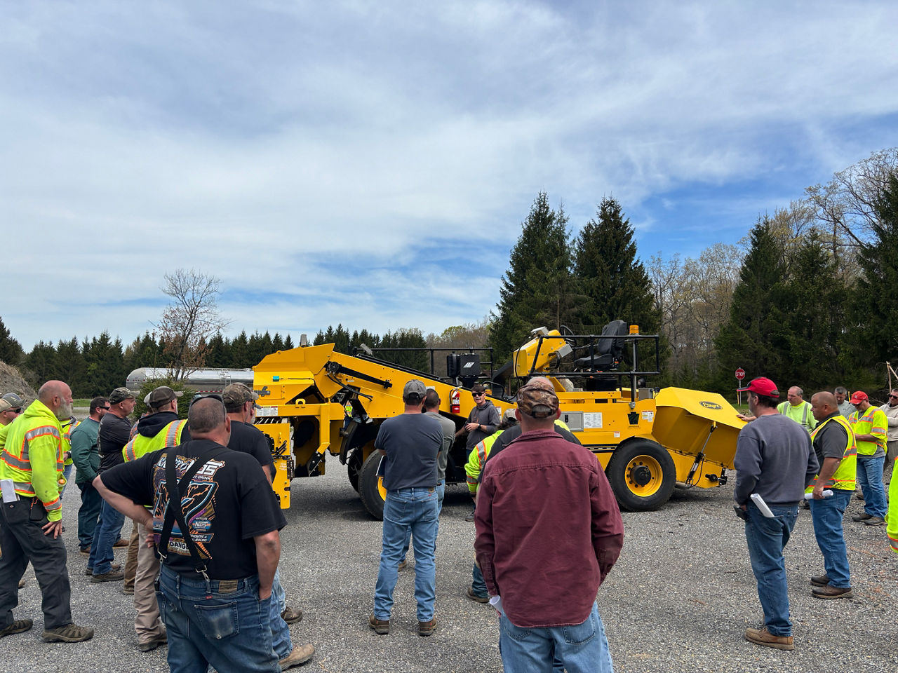 Several roadway maintenance crew members stand around a large of piece of equipment as an instructor stands in front of the piece of equipment discussing proper operation of the equipment.