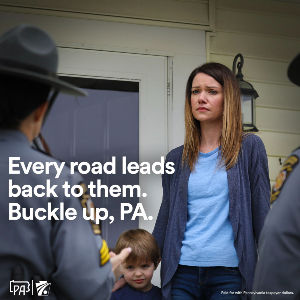 Woman looking distressed with her young son at her side and police at her door. Text overlay reads, “Every road leads back to them. Buckle up, PA.”