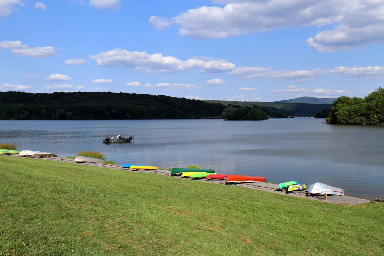 A small motorboat on the lake with many canoes and kayaks moored on the bank of the lake