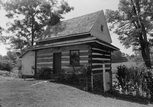 One story log house with a steep roof and hillside setting.