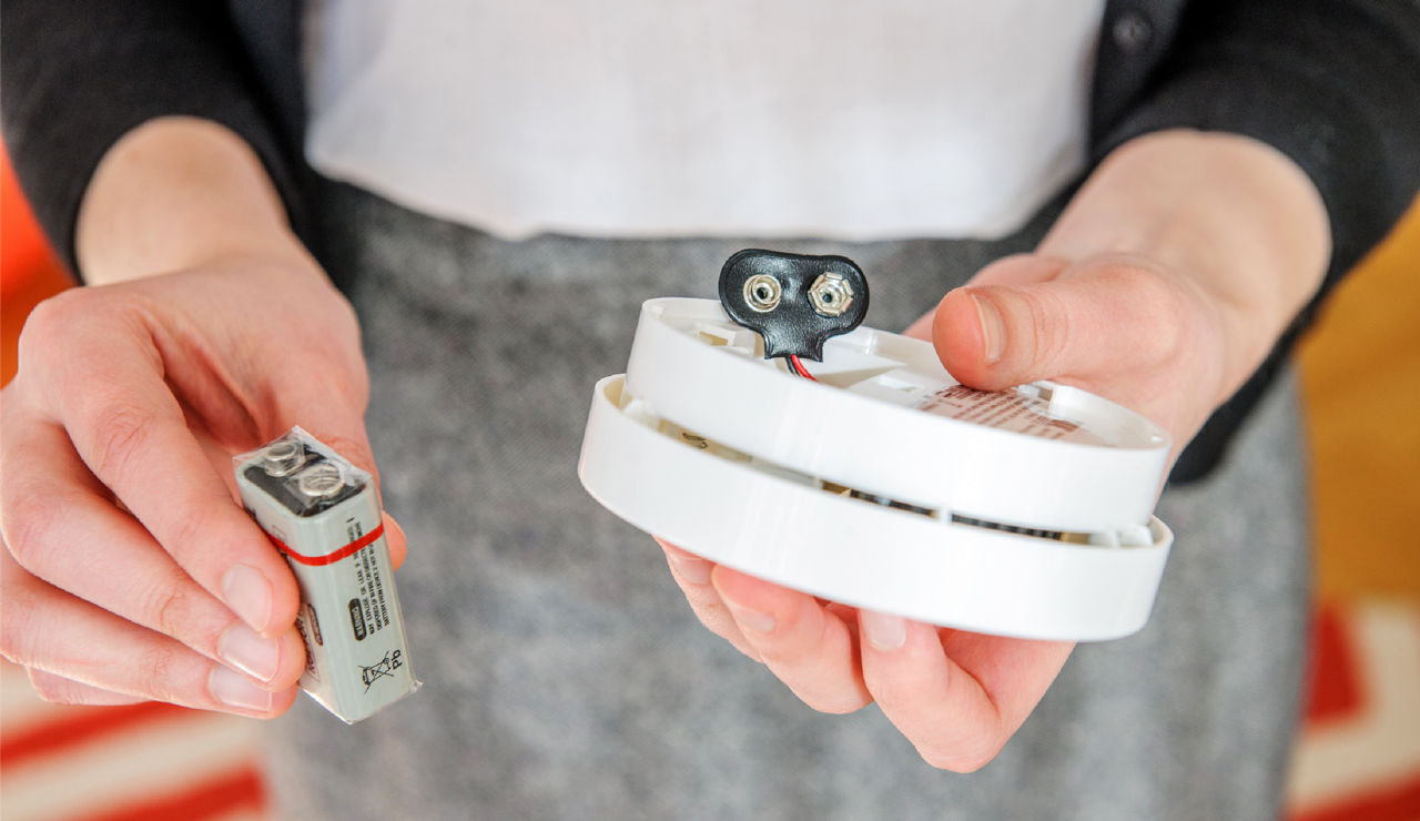 A woman changes the battery in a smoke detector.