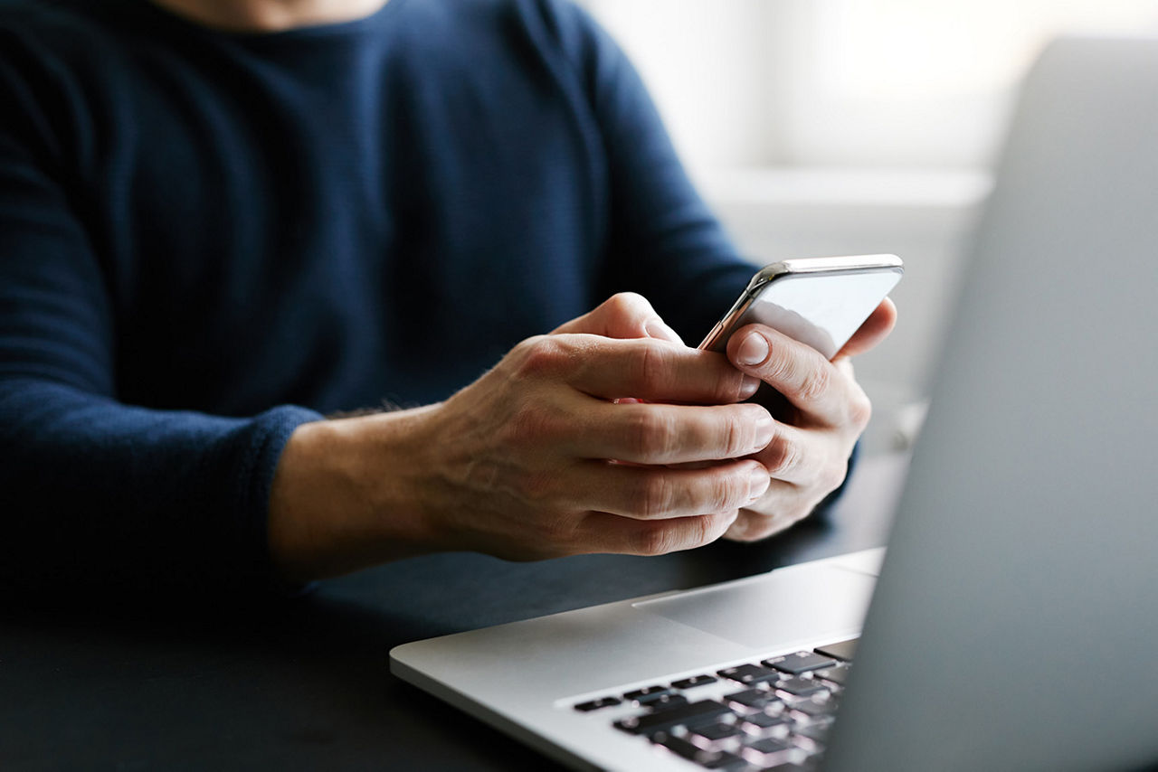 A person looking at a cellphone and laptop