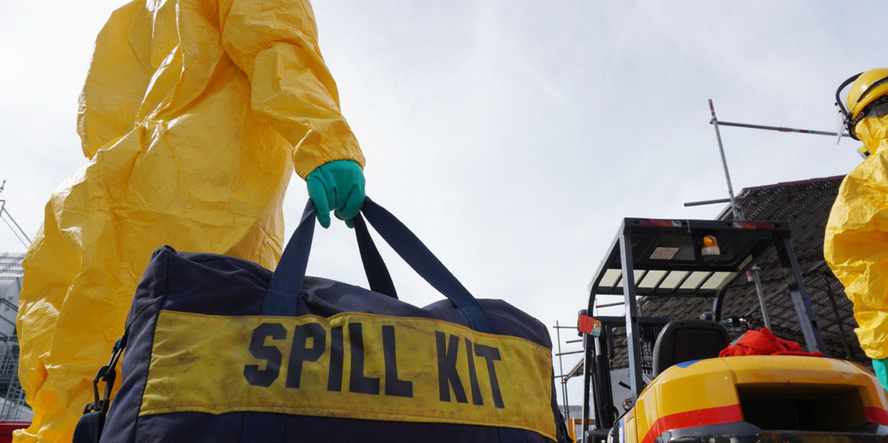 A person in HAZMAT gear carries a spill kit.