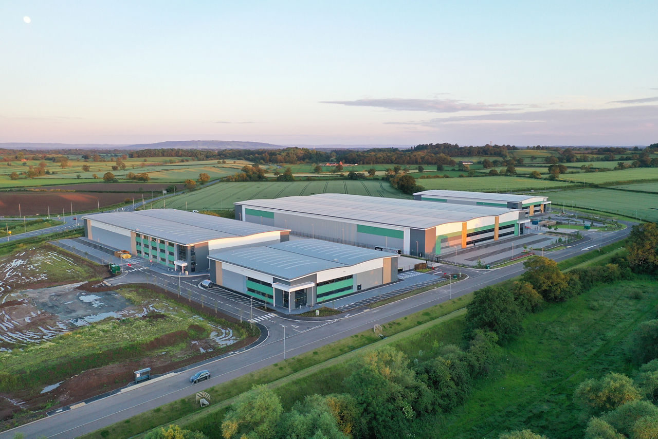 An aerial view of a large industrial facility and warehouse, surrounded by miles of agricultural land