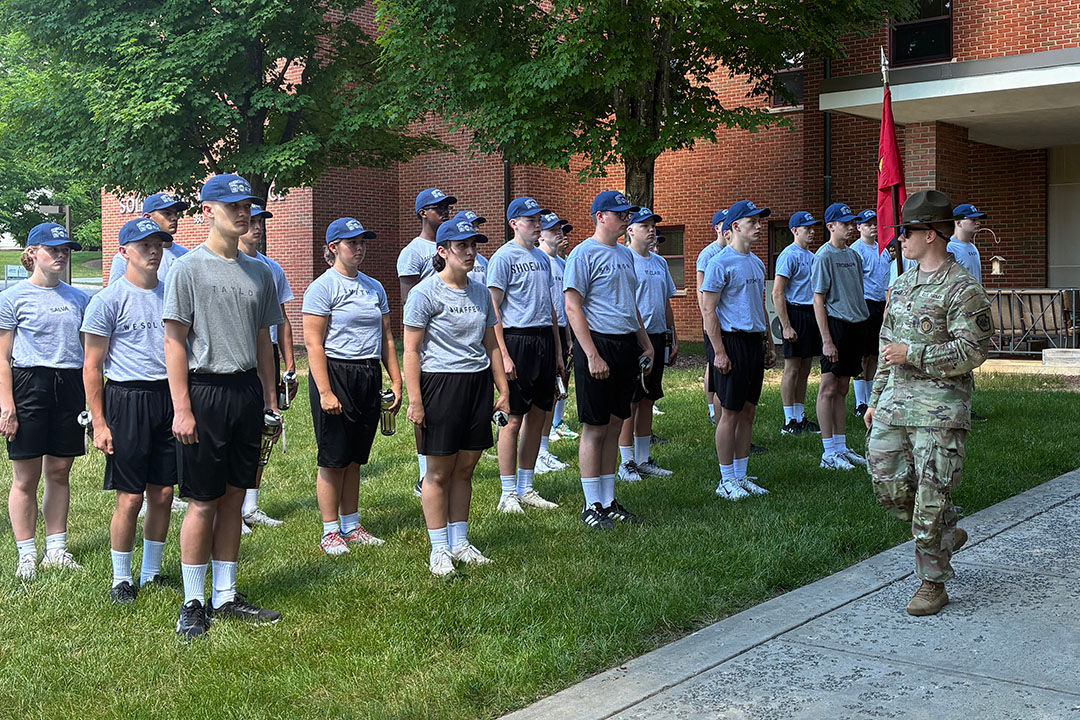 Youths stand in formation at attention outside a building with an Army drill sergeant