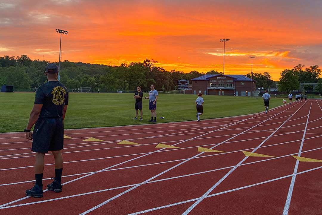 Youths jog on a track while camp instructors observe during a brilliant sunset
