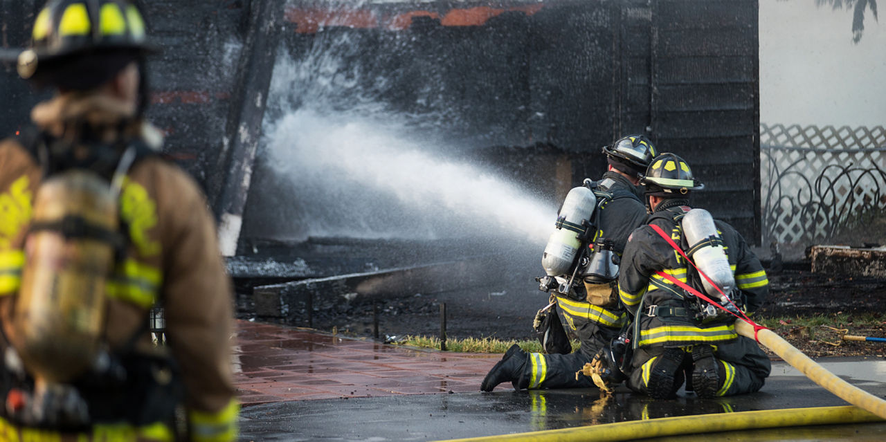 Firefighters kneel while using a hose.