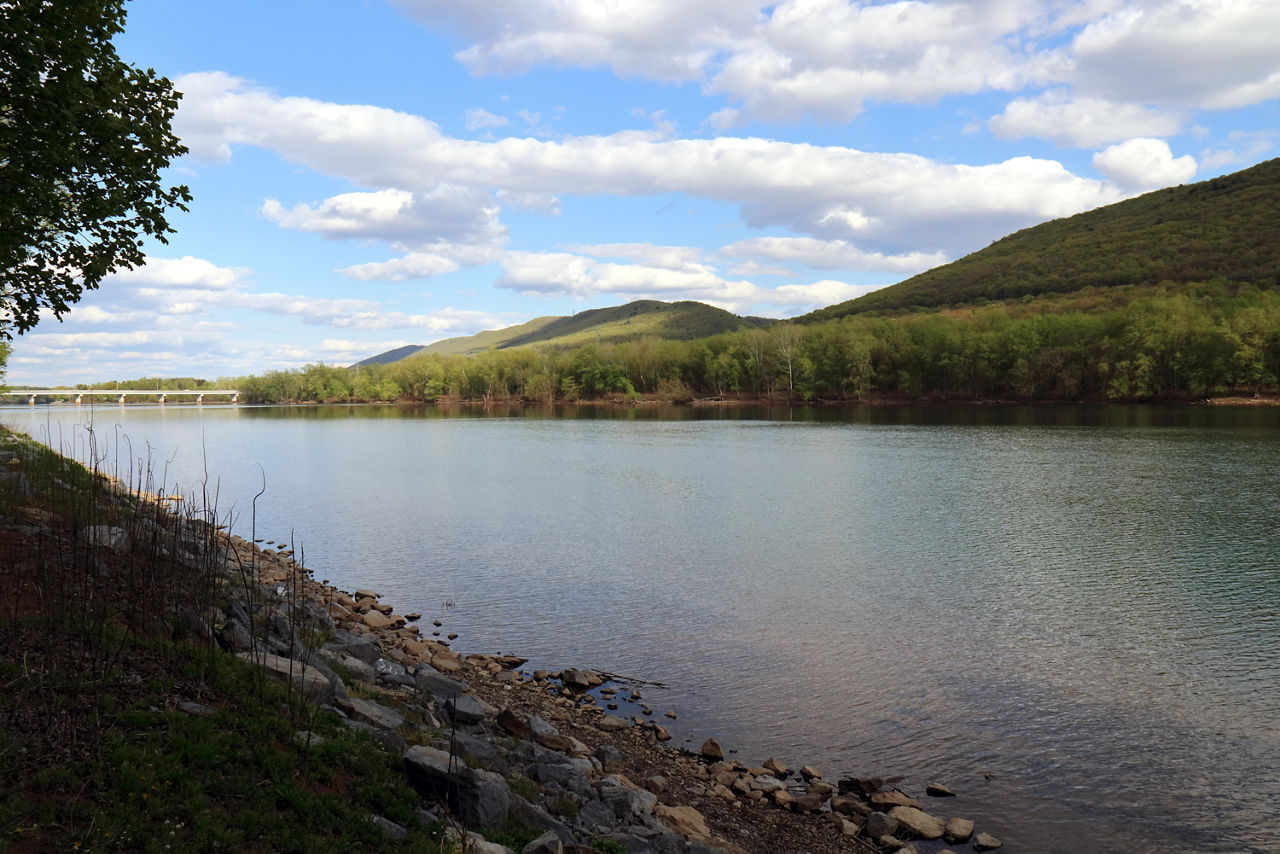 A river with a rocky bank on one side and forested mountains on the other side