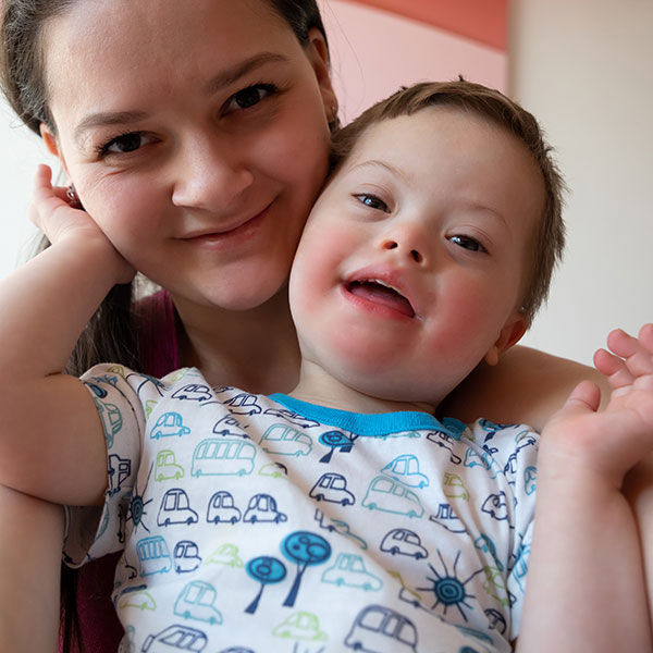 Little boy with special needs touching his mother's face while both are smiling.