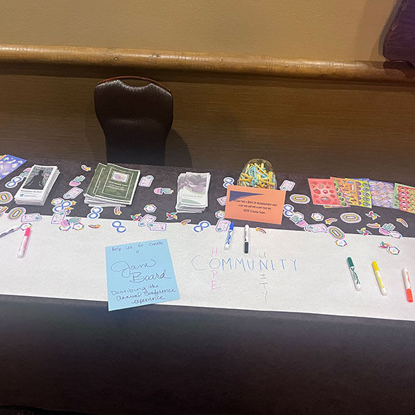 Activity tables including coloring Self-Care Tip Sheets, rock painting, pipe cleaners as fidgets, sensory stickers, a jar of care (mindfulness, self-care, and encouragement notes in a jar that participants could take while passing by), scent stickers, and printed brochures of mindfulness and grounding techniques.