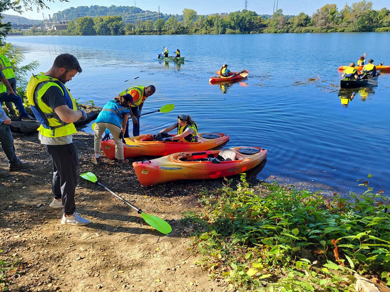 Paddlers wearing life jackets assemble their gear ashore before heading out on the river.