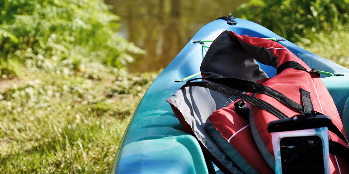 Close-up of the front of a kayak with a life jacket and a cell phone in a dry bag about to launch into a stream.