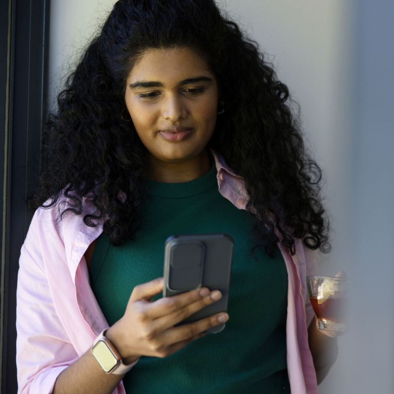 Woman looking at her smartphone while holding a drink.