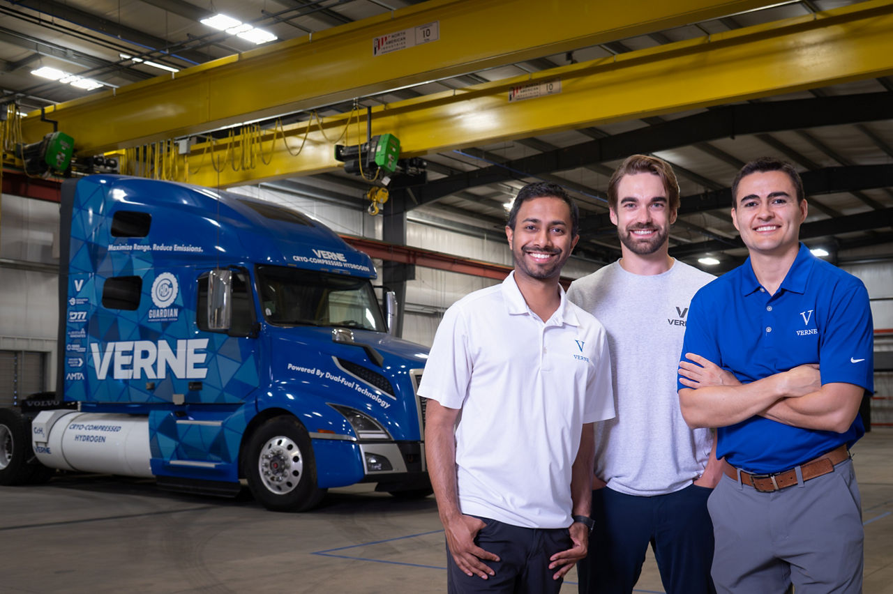 The founders of Verne pose for a photo in front of a blue semitruck, adorned with the company's logo, in a warehouse.