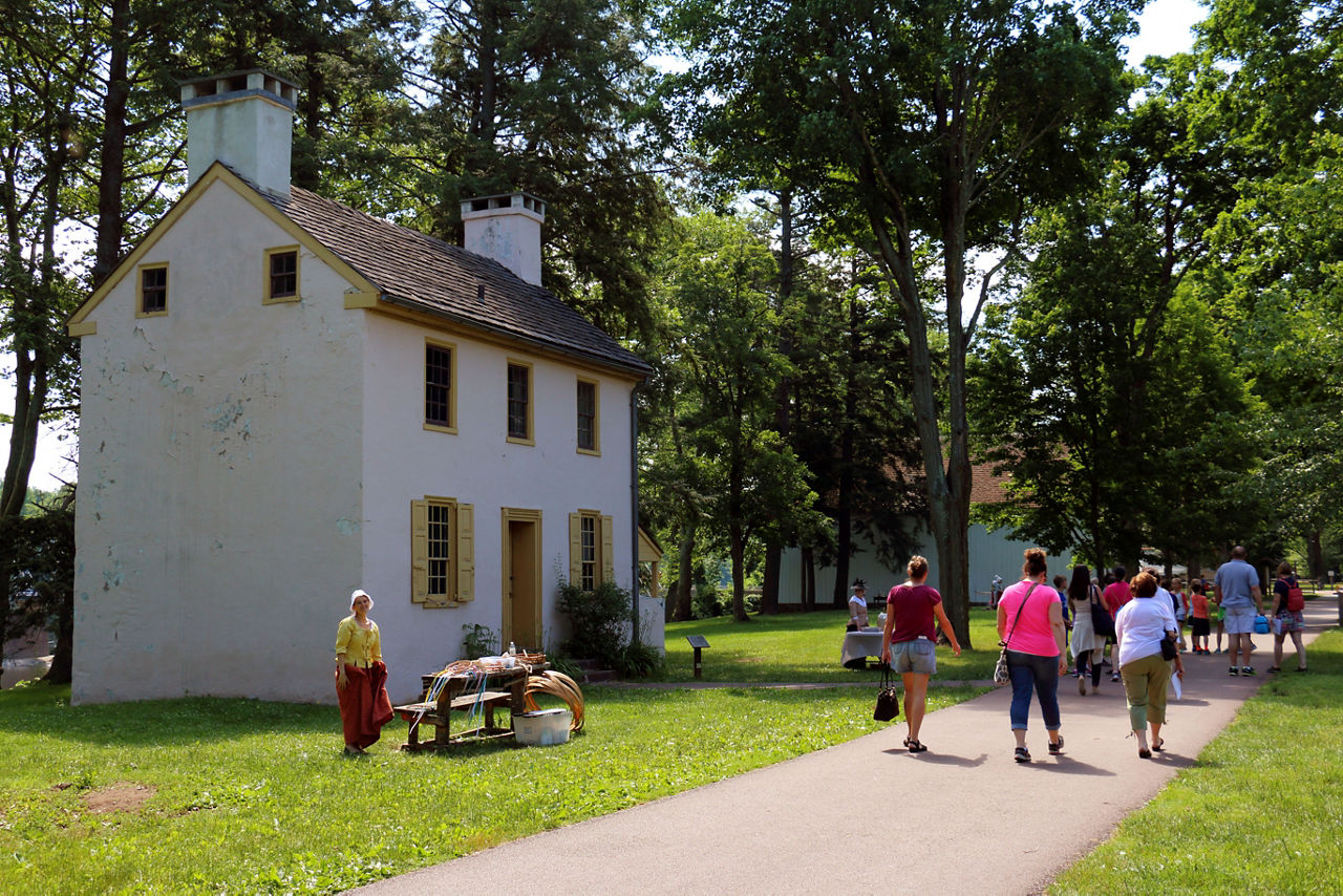 A group of people walking on a paved path past a historic reenactor outside of a historic while building