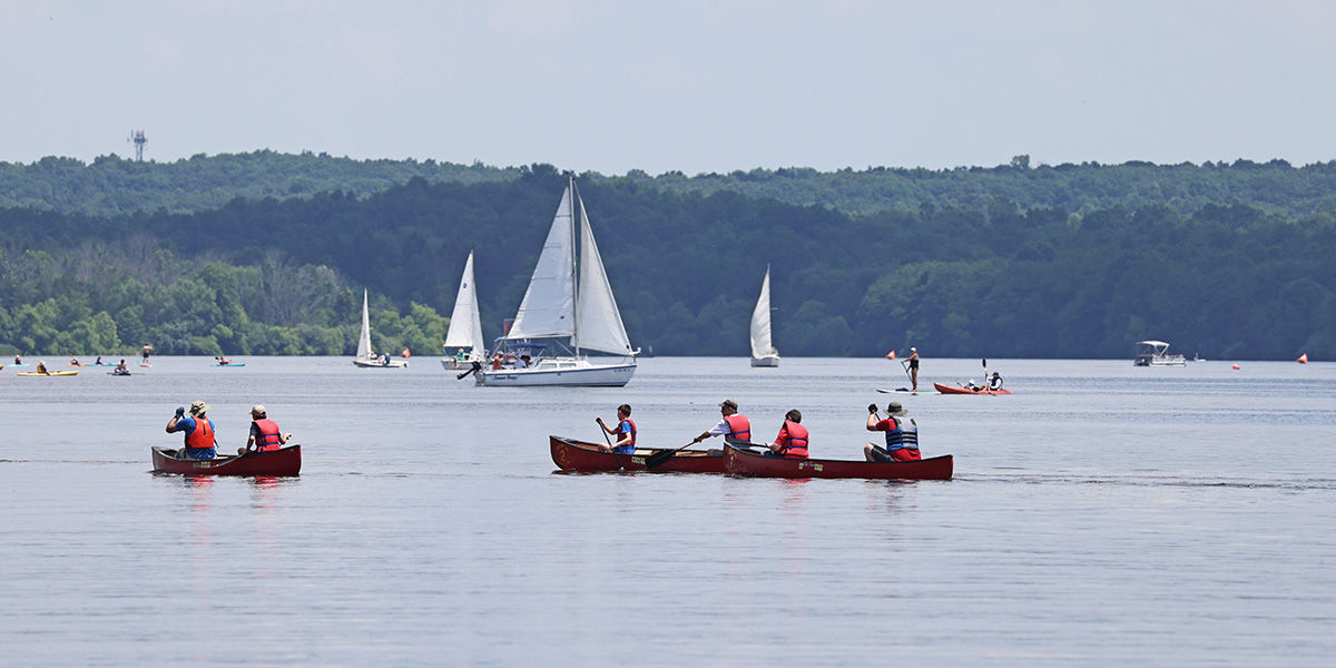 Scenic shot of people where life jackets paddling canoes, kayaks, paddleboards, and sailing on Lake Nockamixon.