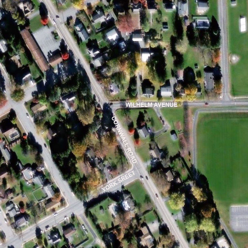 An aerial view of multiple intersecting roadways surrounded by trees, houses and open fields.