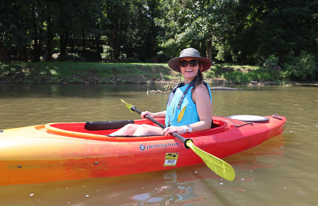 Woman wearing a life jacket, floppy hat and sunglasses while paddling a kayak with a 2027 Launch Permit sticker along the Conestoga River.