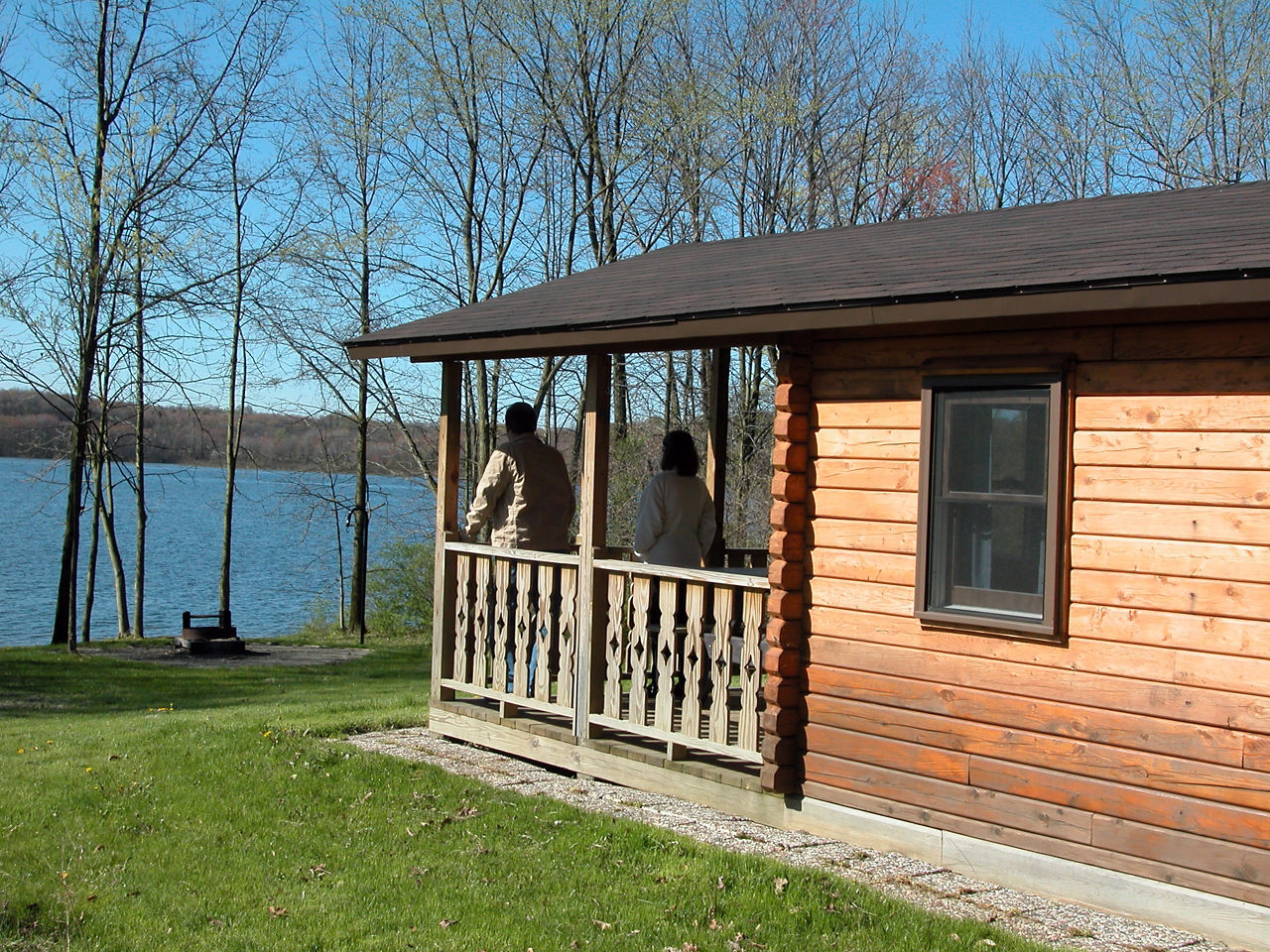 A couple on the porch of a wooden cabin overlooking a lake