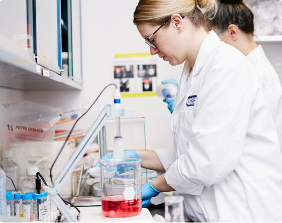 A smiling scientist wearing a lab coat works at her computer in a bright laboratory