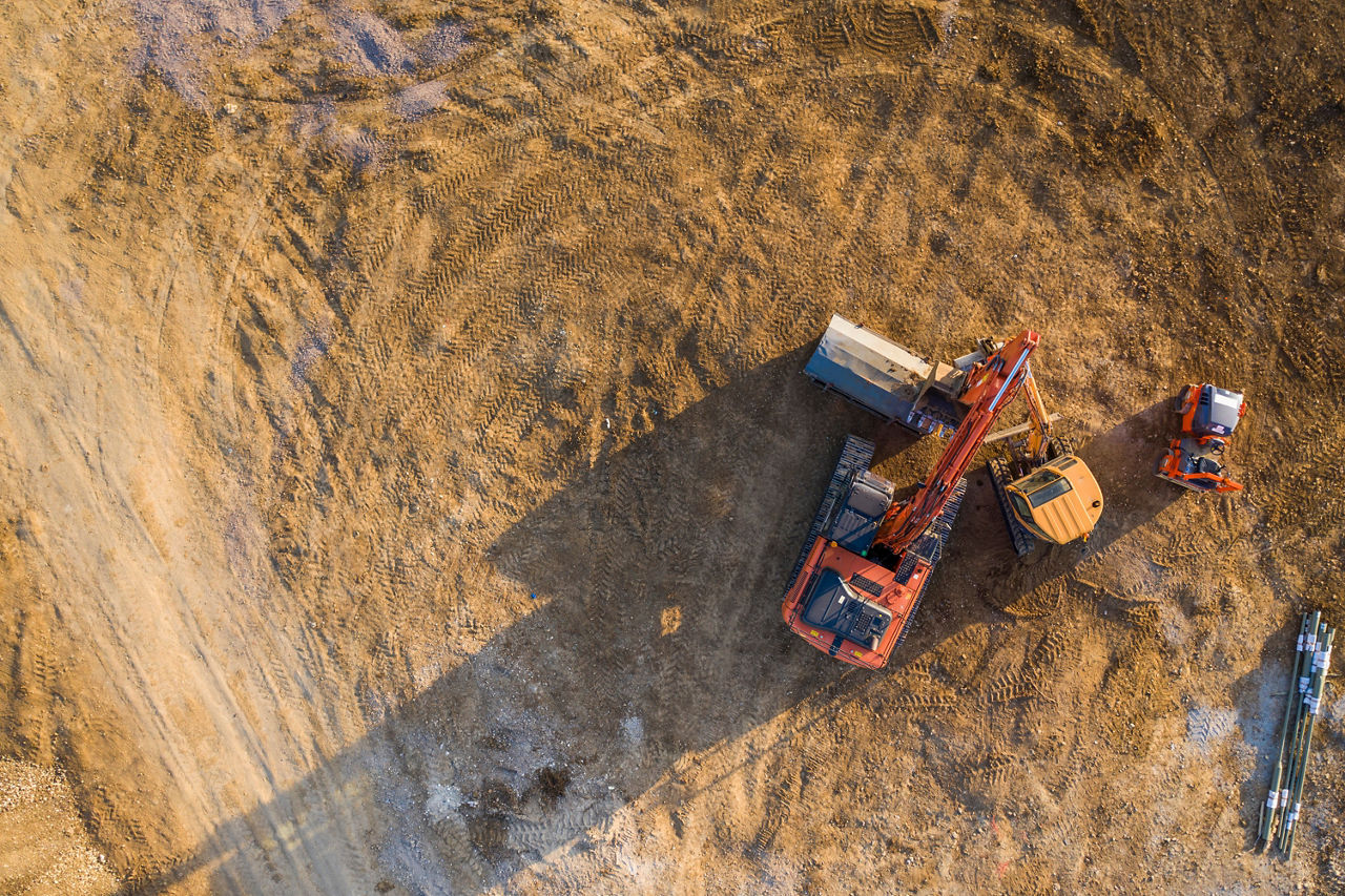 An aerial view of a construction excavator vehicle operating on a dirt lot.