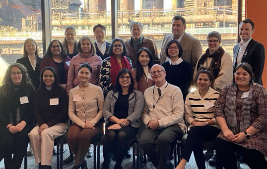 A group of businesspeople pose for a picture in front of a window at a site tour event.